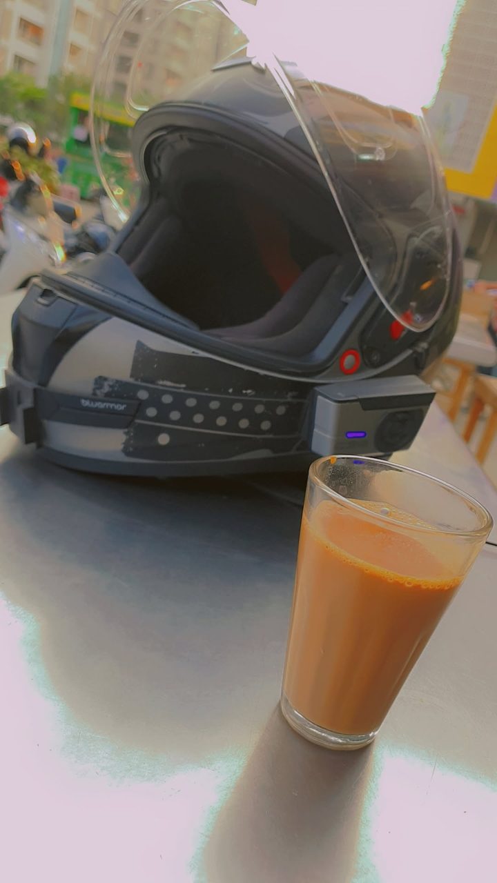 A motorcycle helmet with a Bluetooth headset on a cafe table beside a glass of masala chai