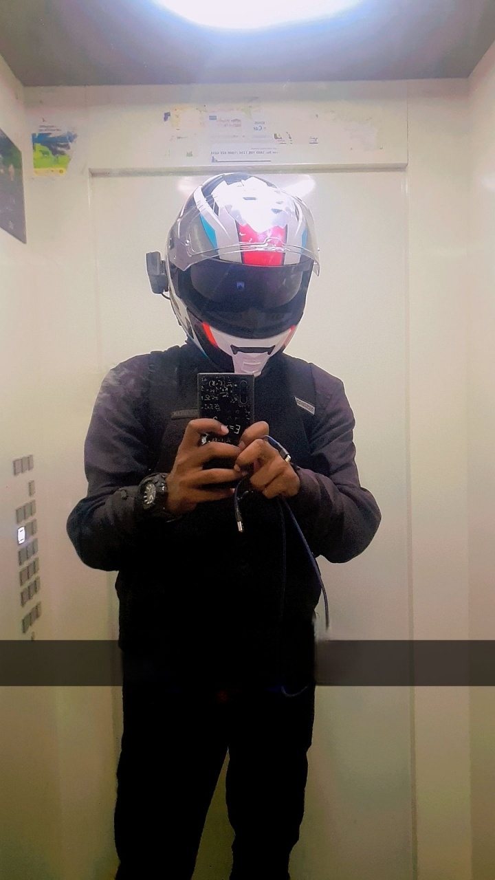A rider in a full-face helmet and riding jacket taking a mirror selfie in an elevator