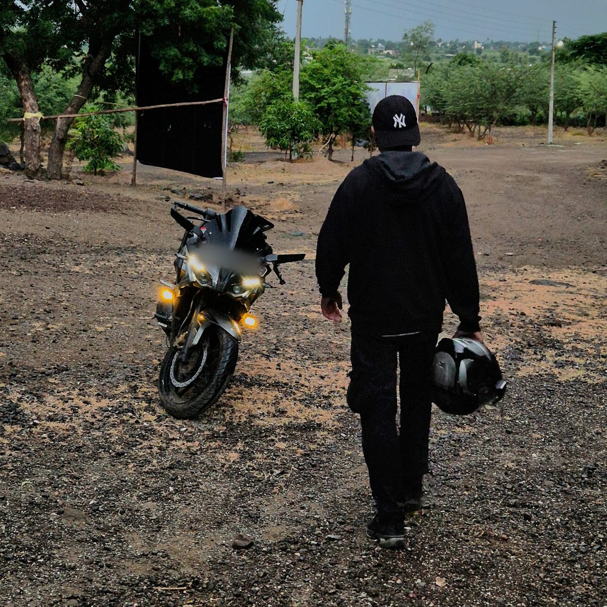 Close view of the motorcycle with its lights on as the rider walks up, carrying a helmet